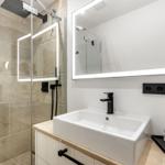Badezimmer mit Dusche, Waschbecken und beleuchtetem Spiegel