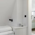 Schlafzimmer mit weißem Bett und integriertem Schrank. Nebenraum mit Dusche und Spiegel.