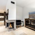 Wohnbereich mit Kamin, Fernseher und Küchenbereich im Hintergrund.