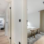 Schlafzimmer mit Bett, Holzbank und Fenster. Flur mit Schreibtisch und Wandbild.