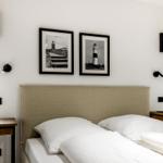 Schlafzimmer mit Bett, zwei Nachttischen und zwei Wandbildern von Leuchttürmen.