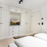 Schlafzimmer mit weißem Schrank, Fernseher und Spiegel.