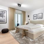 Schlafzimmer mit Bett, Fenster, Wandbildern und Holzboden.