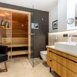 Bad mit Sauna, Waschbecken und Toilette. Glaswand trennt Sauna vom Rest.