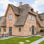 Haus mit strohgedecktem Dach und Steinmauer. Außenterrasse mit Tisch und Stühlen.