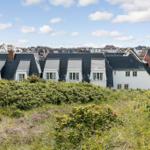 House with dark roof and white windows on a green hillside.