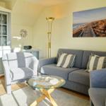 Living room with sofa, armchairs, and glass table. Wall art shows beach path.
