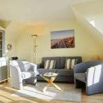 Living room with sofa, two chairs, and glass table. Wall picture shows beach. Wooden floor and vaulted ceiling.
