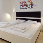 Double bed with white bedding, two nightstands with lamps and wall art with elephants.