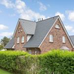 A two-story house with red brick walls and gray roof. Front garden with green hedge fence.