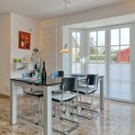 Dining area with table, chairs, and window front. Tile floor and wall shelf visible.