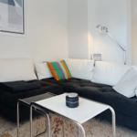 Black sofa with white cushions and colorful cushion. Table with candle and floor lamp.