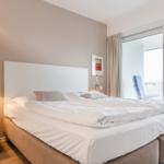 A bedroom with a double bed, desk, and balcony view.