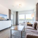 Living room with sofa, coffee table, and TV. View to balcony with landscape view.