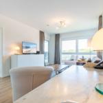 Living area with TV, sofa, and balcony view. Bedroom with bed in background.