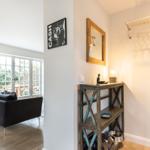 Living area with sofa and windows. Entryway with table, mirror, and coat rack.