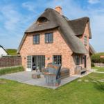 Red brick house with thatched roof and terrace with garden furniture.