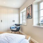 Bedroom with bed, wardrobe, and chair. Windows with view of outside area.
