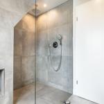 Shower cabin with glass wall and shower head. Niche with glass dome and white vase.