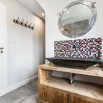 Bathroom with wooden vanity, mosaic wall, and round mirror.