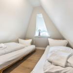 Two beds with white linens and towels under a skylight.