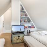 Room with double bed, TV, and bookcase under sloped ceiling.