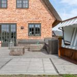 Terrace with wooden furniture and beach chair in front of brick house with sliding doors.