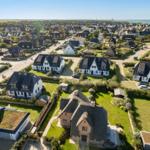 Aerial view of a coastal village with traditional houses and green lawns.
