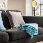 A dark sofa with blue cushions and a blanket.