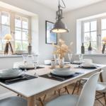 Dining room with table, chairs, and windows. Table set with dishes and glasses.