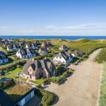 Houses by the sea with green areas and sandy path.