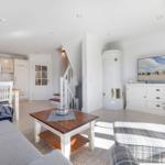 Wohnzimmer mit Sofa, Sessel und Kamin. Küche und Treppe sind sichtbar.