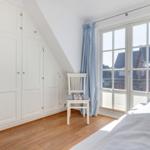 Schlafzimmer mit weißem Schrank, Stuhl und Fenster mit Blick auf Gebäude.