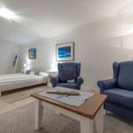 Schlafzimmer mit Bett, zwei blauen Sesseln und Wandbildern.