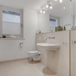 Badezimmer mit Toilette, Waschbecken und Dusche. Fenster mit Jalousie und Handtuchhalter.