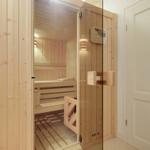 Sauna mit Holzverkleidung und Glasfront. Innere Bänke und Heizgerät sichtbar.