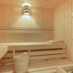 Holzsauna mit Sitzbänken, Eimer und Thermometer an den Wänden.