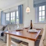 Esstisch mit Stühlen, Fenster mit Vorhängen und Sofa im Hintergrund.