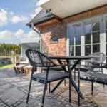 Terrasse mit Tisch und Stühlen vor einem Haus mit Backsteinwand und Fenstern.