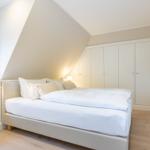 Schlafzimmer mit Dachschräge, Bett, Kleiderschrank und Fenster.