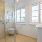 Badezimmer mit Dusche, Toilette und Waschbecken. Fenster mit Blick nach draußen.