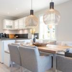 Essbereich mit Holztisch, Stühlen und modernen Hängelampen. Küche im Hintergrund.
