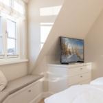 Schlafzimmer mit Fensterbank, TV und Bett unter Dachschrägen.