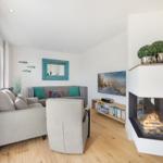 Wohnzimmer mit Sofa, Sessel, Kamin und Fernseher.
