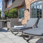 Terrasse mit Liegen, Tisch und Stühlen vor Backsteinhaus mit Dachziegeln.