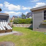 Garten mit Strandkorb, Holzhaus und Blumenkasten unter blauem Himmel.