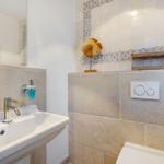 Badezimmer mit Waschbecken, Spiegel und Toilette. Wandfliesen mit blau-weißem Muster.