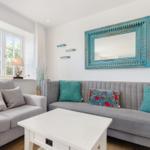 Ein Wohnzimmer mit grauem Sofa, blauem Spiegel und Fensterblick.