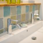 Waschbecken mit Chromarmatur und farbigen Fliesenwand.