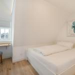 Schlafzimmer mit Bett, Schreibtisch und Wandbild mit Seepferdchen.